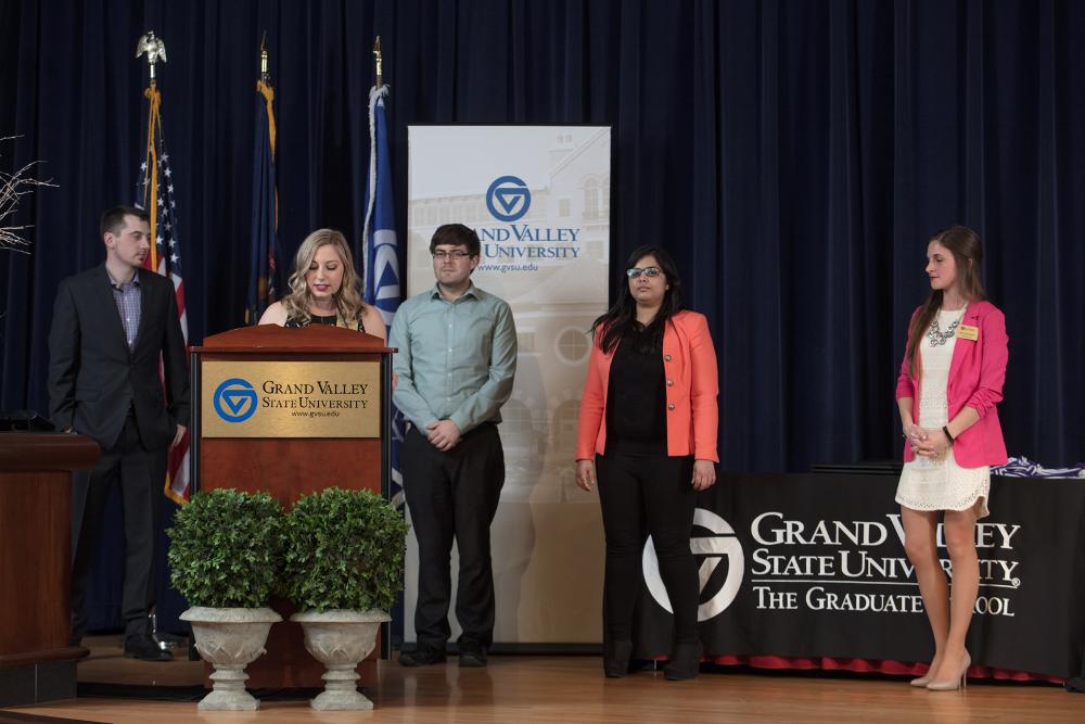GSA E-board standing on stage while the president speaks at a podium